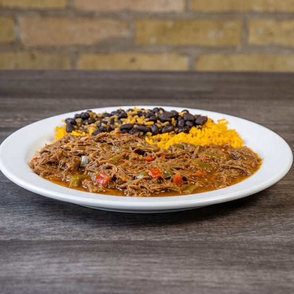 A plate of shredded beef with red and green peppers, yellow rice, and black beans.
