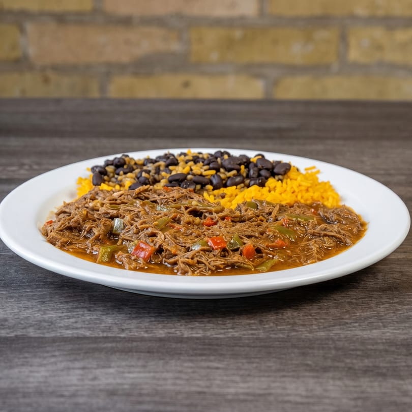 A plate of shredded beef with red and green peppers, yellow rice, and black beans.