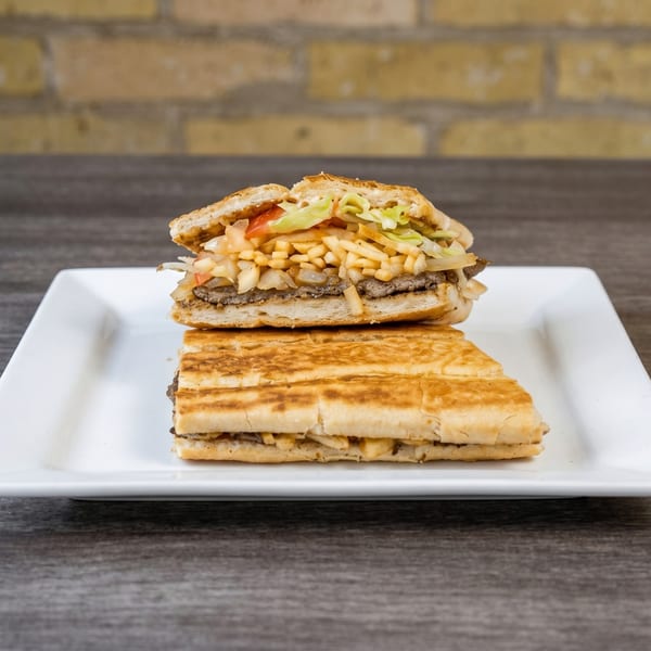 Two halves of a pressed Cuban sandwich, filled with meat, cheese, lettuce, and fries, on a white plate.