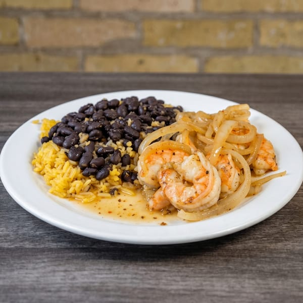 Shrimp with sautéed onions, yellow rice, and black beans on a white plate.
