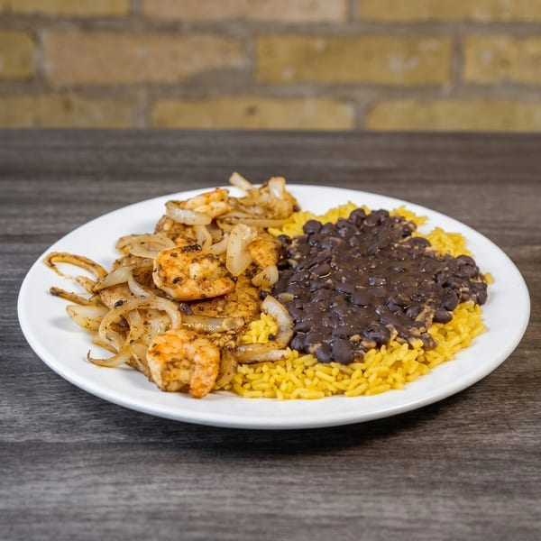 Shrimp and onions with yellow rice and black beans on a white plate.