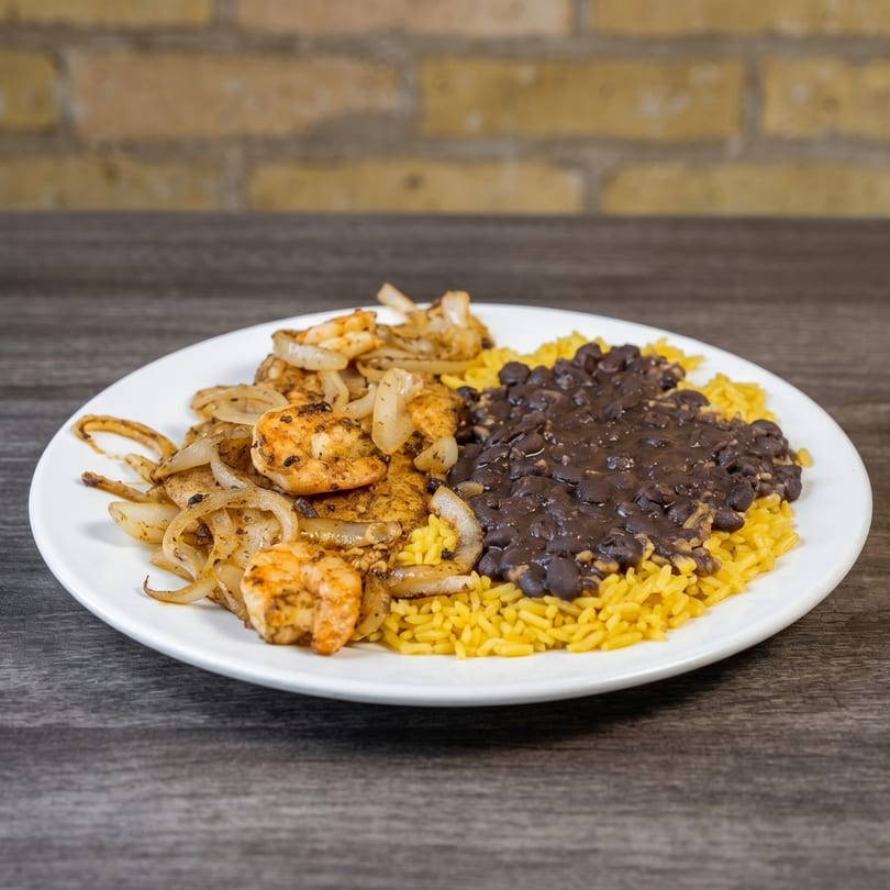 Shrimp and onions with yellow rice and black beans on a white plate.