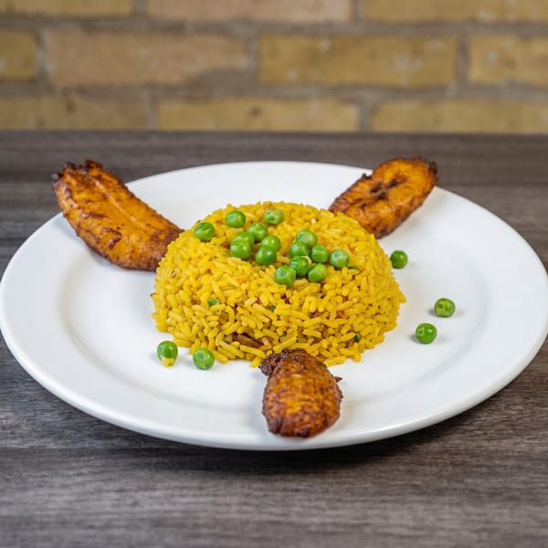 Yellow rice with green peas and fried plantains on a white plate.