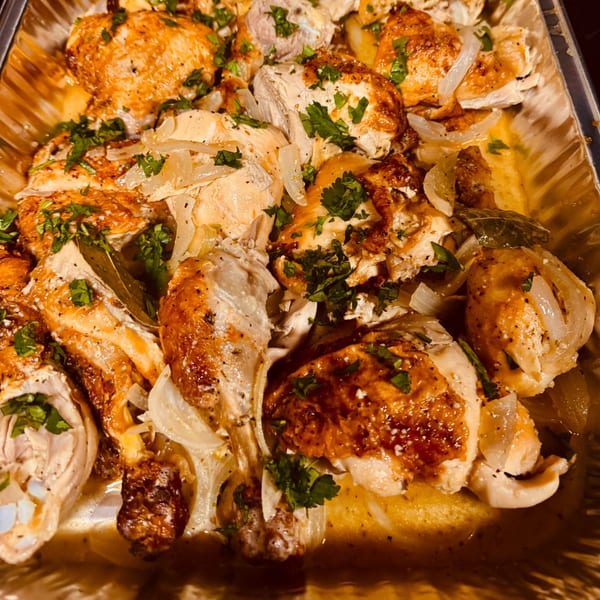 Close-up of roasted chicken pieces with onions and parsley in a foil pan.