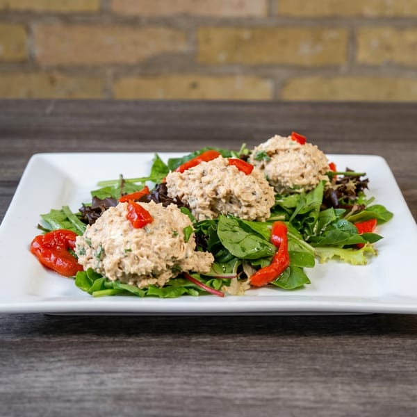 Three scoops of tuna salad on a bed of mixed greens with red pepper garnish.
